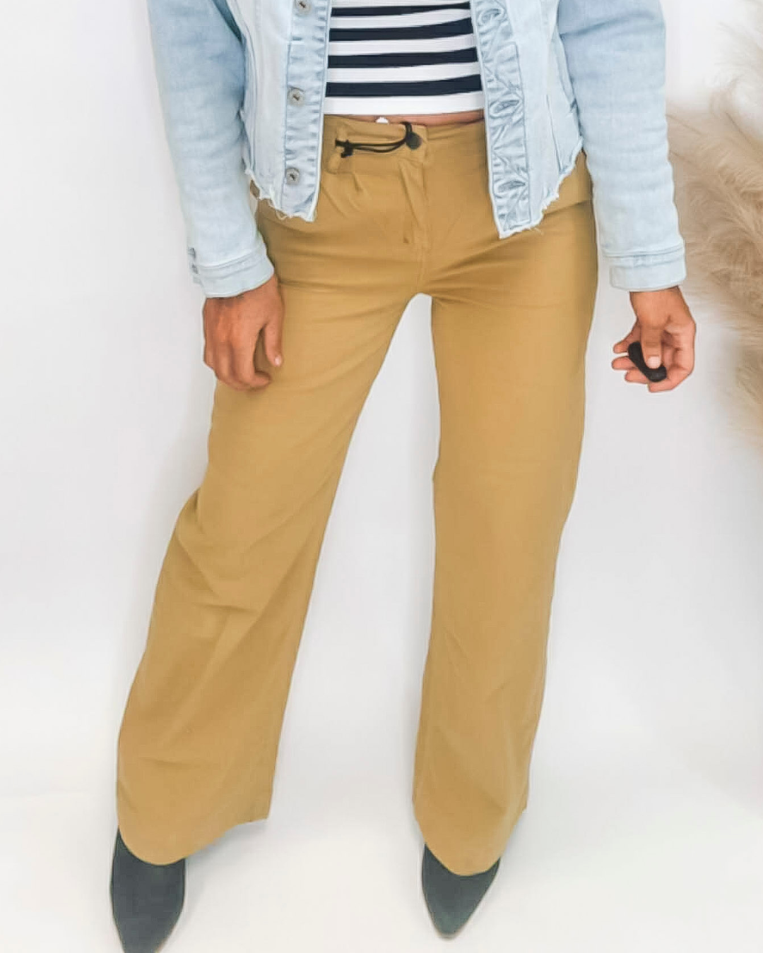 Person wearing mustard yellow pants with a light blue denim jacket and striped shirt on a white background