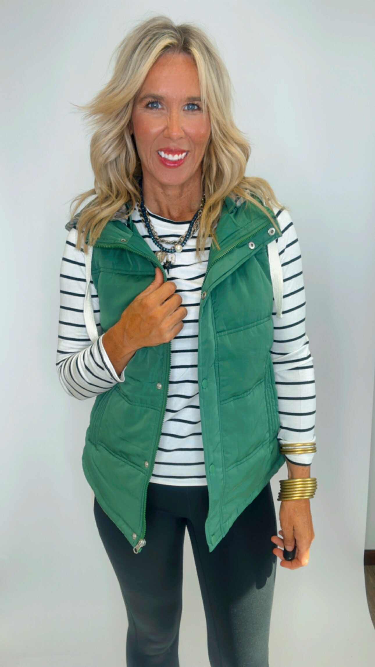 Woman wearing a green puffer vest over a striped shirt on a white background