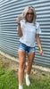 Woman in a white t-shirt and denim shorts standing in front of a metal wall.