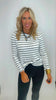 Woman wearing a black and white striped long-sleeve top and dark pants against a plain background