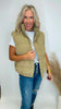 Woman wearing a beige vest, striped shirt, and jeans against a white background