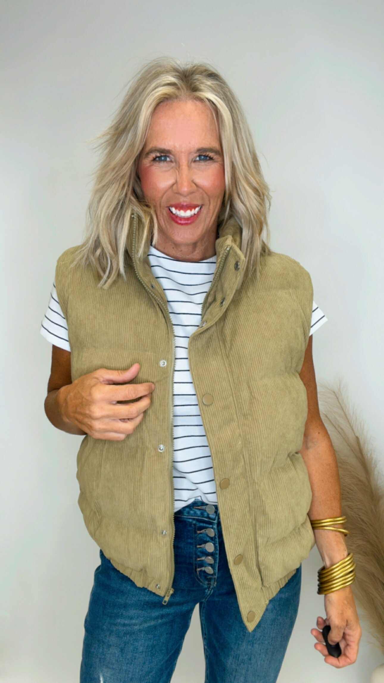 Woman wearing a green vest over a striped shirt with a plain background