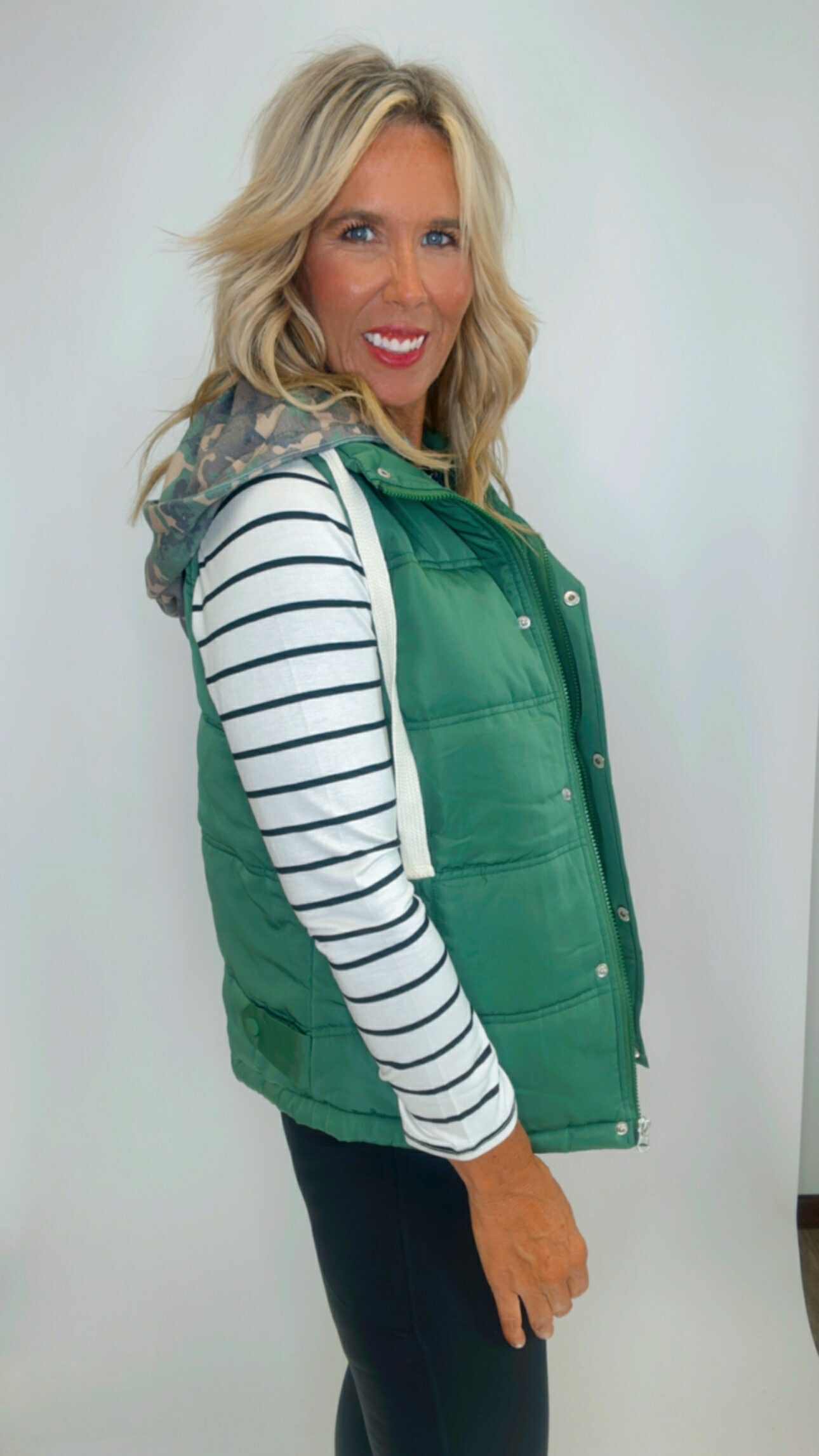 Woman wearing a green puffer vest over a striped shirt against a white background