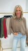 Woman wearing a brown sweater and light blue jeans standing in front of a rack of sweaters.