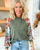Woman wearing a green ribbed sweater with floral sleeves in a home setting.