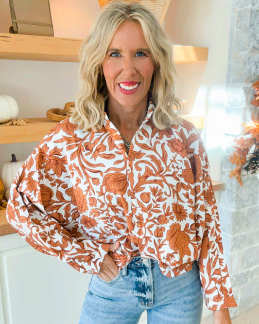 Woman wearing a floral blouse with orange and white pattern in a home setting.