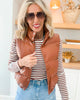 Woman wearing a brown puffer vest over a striped shirt with sunglasses indoors.
