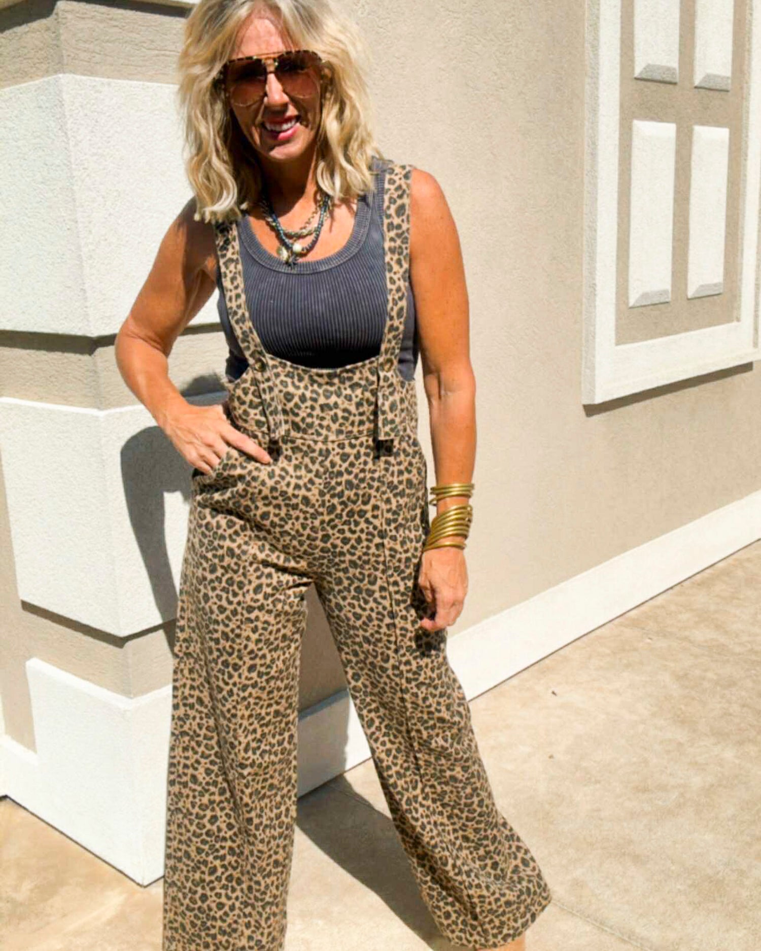 Woman wearing leopard print overalls and sunglasses outdoors.