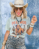 Woman wearing a light green t-shirt with a graphic design, leopard print skirt, and straw hat against a textured blue background.