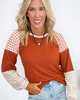 Woman wearing a brown and white checkered long-sleeve top with a plain background