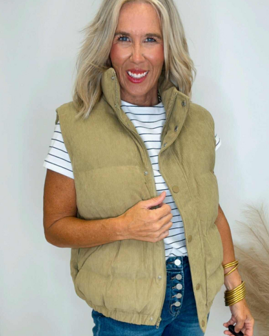 Woman wearing a green vest over a striped shirt with a plain background