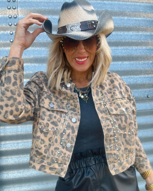 Person wearing a leopard print jacket and cowboy hat against a corrugated metal background