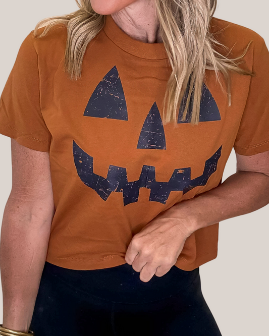 Person wearing a brown t-shirt with a jack-o'-lantern face design.