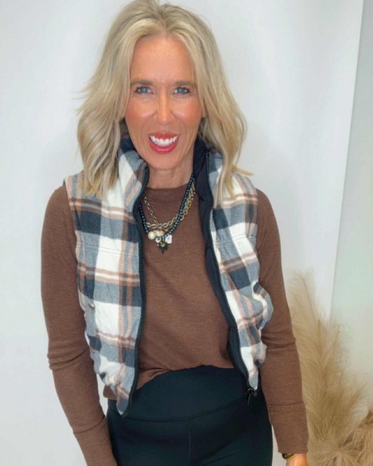 Woman wearing a plaid scarf, brown sweater, and dark pants against a white background