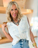 Woman wearing a white sleeveless top with lace details and denim shorts indoors.