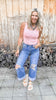 Woman wearing a pink top and ripped jeans standing in front of a wooden wall.