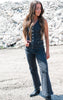 Woman wearing a denim outfit with a button-up top and flared jeans standing on a rocky surface.