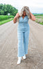 Woman wearing a light blue denim jumpsuit on a rural road.