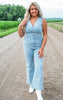 Woman wearing a light blue denim jumpsuit standing on a rural road.