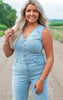 Woman wearing a light blue denim jumpsuit standing on a road with greenery in the background