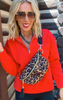 Woman wearing a red jacket with a leopard print bag against a wooden background