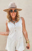 Sleeveless ribbed knit romper in a soft beige tone, styled with stacked bangles and a sun hat