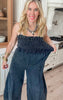 Black sleeveless jumpsuit featuring a smocked bodice and relaxed wide-leg fit, styled in a modern kitchen setting.