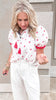 Lightweight white blouse with whimsical strawberry accents paired with casual linen trousers for a fresh, airy look.