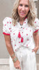 Woman wearing a white gauze top with delicate red strawberry embroidery, paired effortlessly with flowy white linen pants.