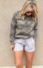Woman wearing light heather grey drawstring fleece shorts with side slits and pockets, paired with a camo sweatshirt.