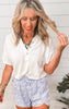 Woman wearing a white blouse and light blue shorts with a white wooden background