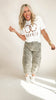Woman wearing a white t-shirt with text and leopard print pants on a plain background
