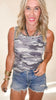 Woman wearing a camouflage tank top and denim shorts on a beige background