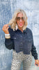 Woman wearing a denim jacket and leopard print pants against a textured wall.