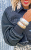 Person wearing a black textured jacket with gold bangles on a blurred background