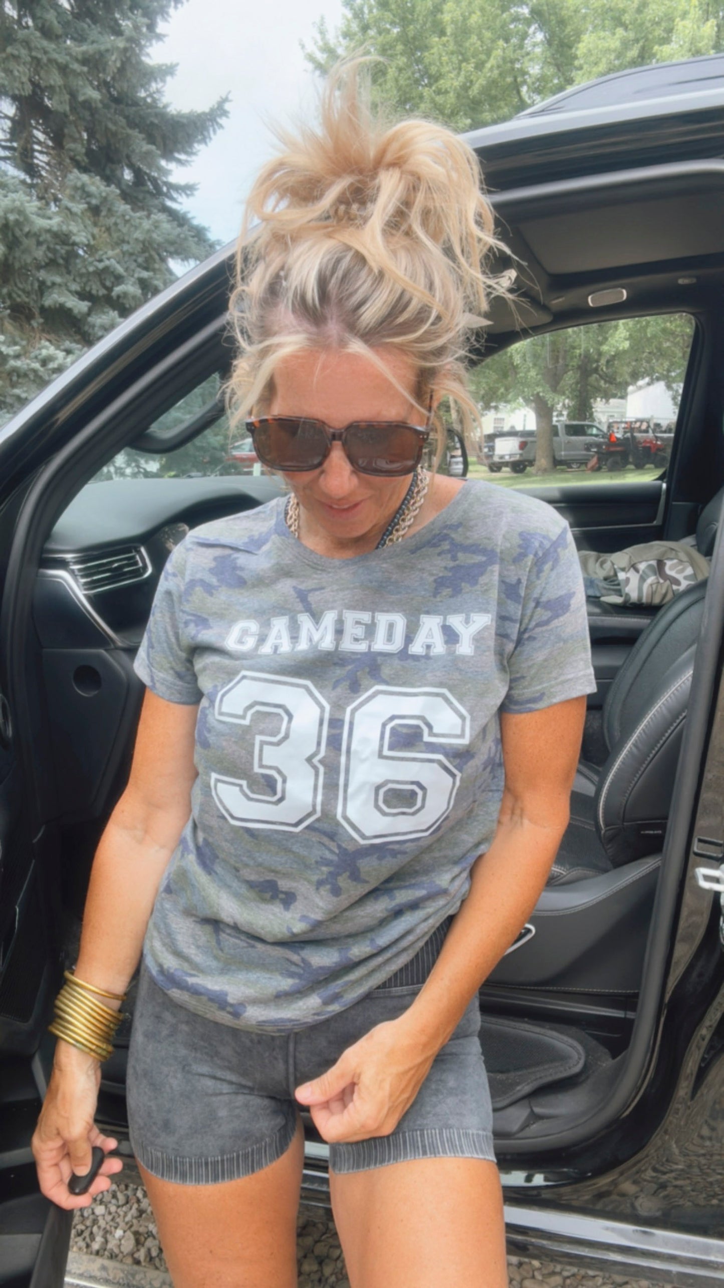 Woman wearing a 'GAMEDAY 36' t-shirt standing next to a car.