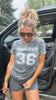 Woman wearing a 'GAMEDAY 36' t-shirt standing next to a car.