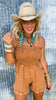 Woman wearing a brown romper and straw hat against a textured wall.