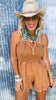 Woman wearing a brown romper with accessories against a textured blue background