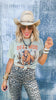 Woman wearing a graphic t-shirt with a cowboy design and leopard print pants against a textured blue background.