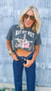 Woman wearing a graphic t-shirt and sunglasses against a textured wall.