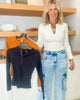 Woman holding a navy shirt with a hanger, standing next to a wooden shelf with decor items.