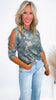 Woman wearing a camouflage top with cut-out sleeves and light blue jeans on a white background