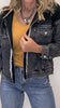 Person wearing a black denim jacket, mustard yellow top, and blue jeans on a plain background