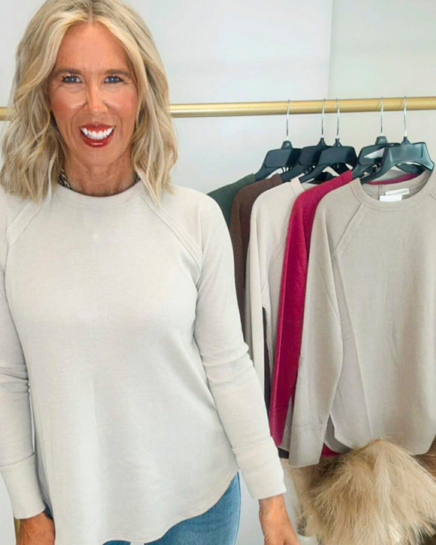 Woman wearing a white sweater standing in front of a rack of sweaters.