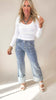 Woman wearing a white long-sleeve top and blue jeans against a plain background