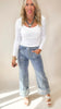 Woman wearing a white long-sleeve top and light blue jeans against a plain background