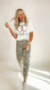 Woman wearing a white t-shirt with text and leopard print pants on a plain background