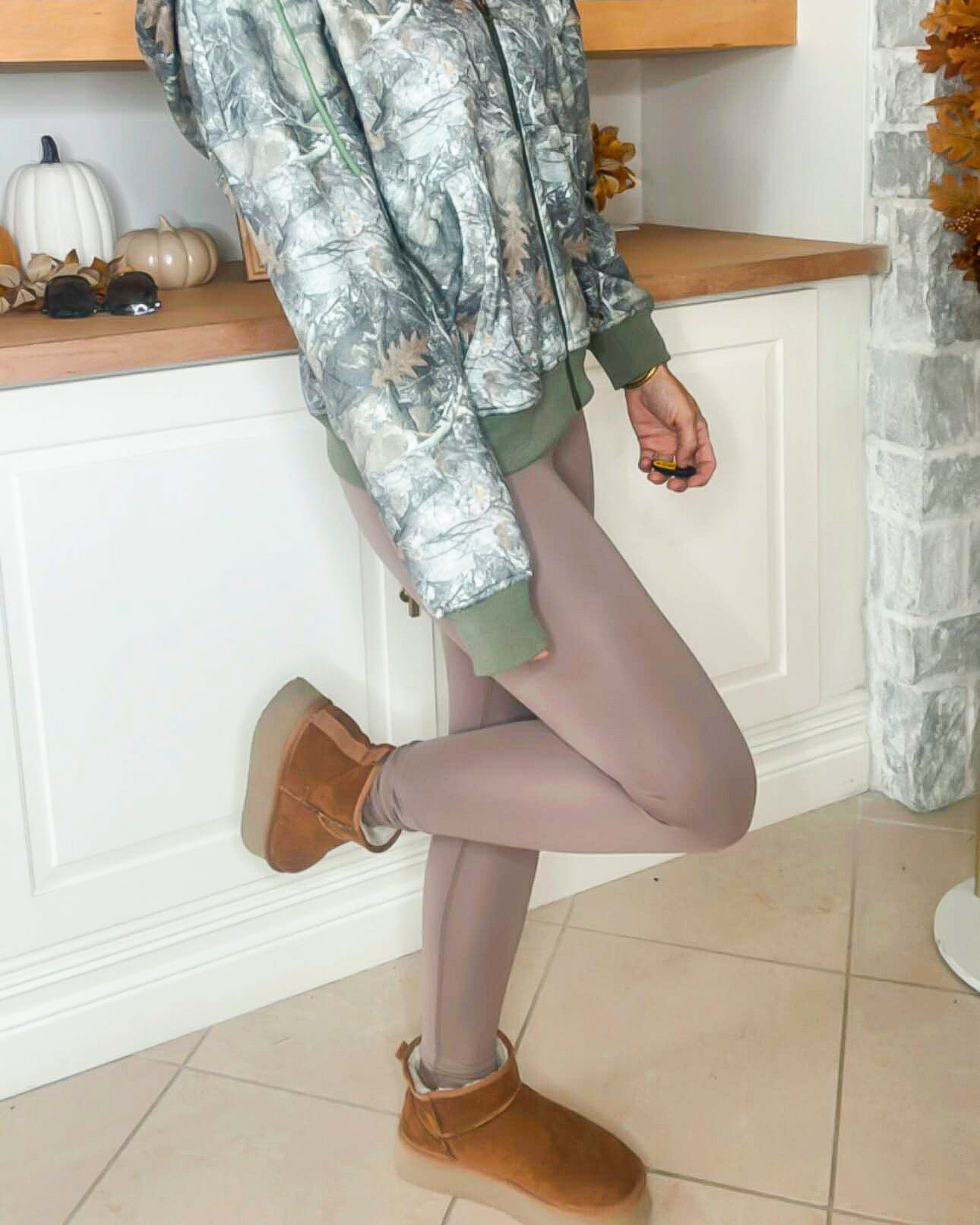 Person wearing a camouflage jacket, beige leggings, and brown boots in a kitchen setting.