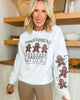 Woman wearing a white sweatshirt with gingerbread design and text in a home setting.